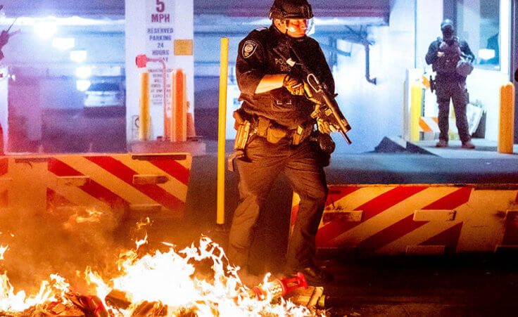 A Department of Homeland Security officer emerges from the Mark O. Hatfield United States Courthouse after demonstrators lit a fire on Sunday, Aug. 2, 2020, in Portland, Ore.