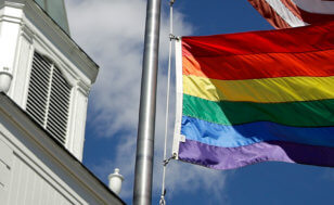 A gay pride flag waves besides a church.