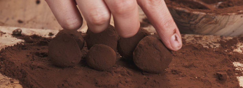A hand rolls balls of chocolate on top of a chocolate-powder-drenched cutting board.