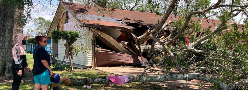 Two people look at the aftermath of Hurricane Laura, as a large tree has demolished their home.