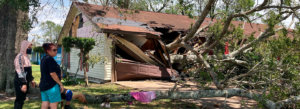 Two people look at the aftermath of Hurricane Laura, as a large tree has demolished their home.