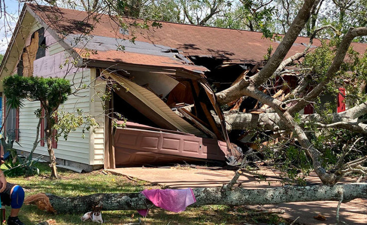 Two people look at the aftermath of Hurricane Laura, as a large tree has demolished their home.