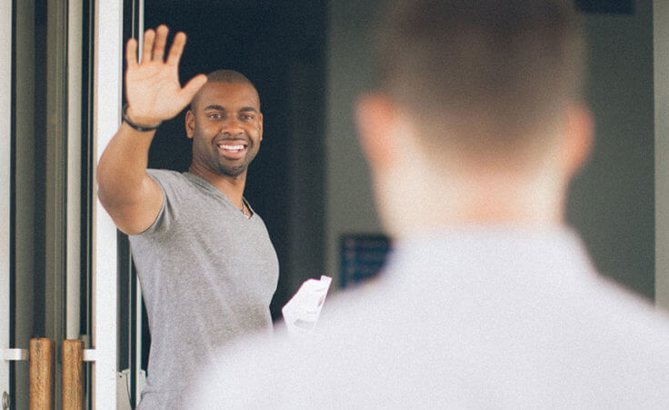 A man standing in front of open church doors waves to an oncoming visitor.