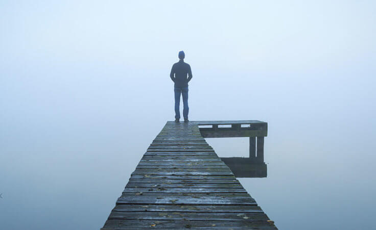 A man stands alone on a dock in a foggy lake