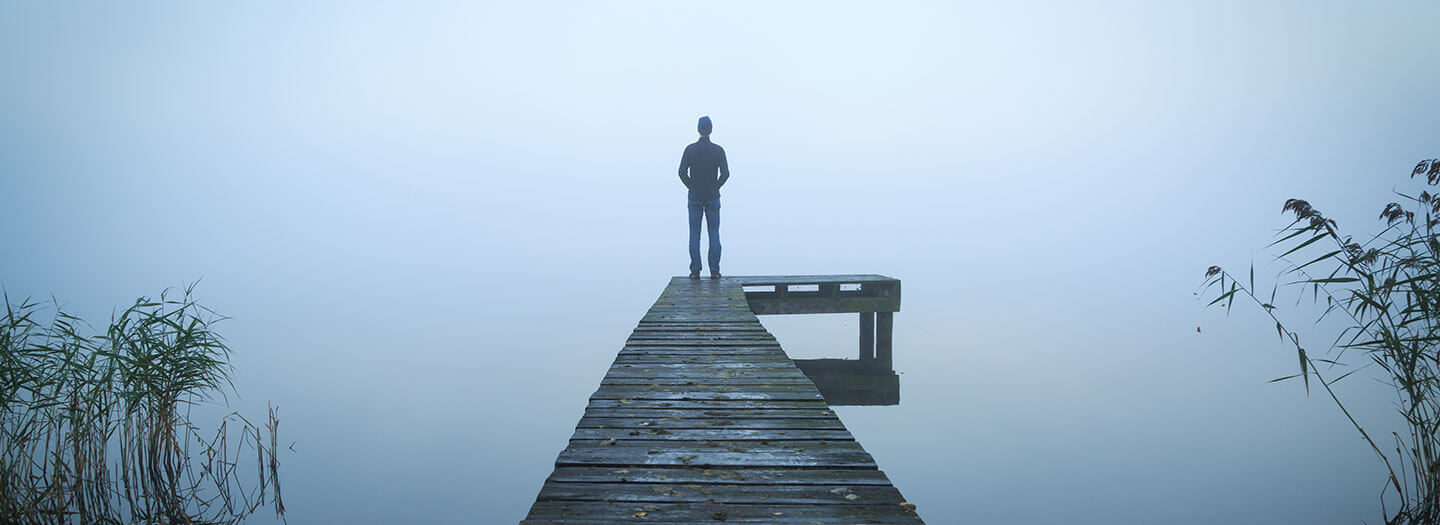 A man stands alone on a dock in a foggy lake