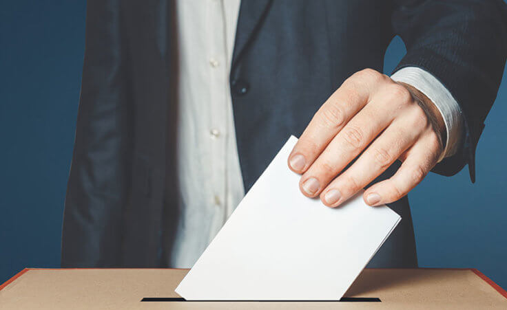 Closeup on a man's hand placing a ballot into a voting box