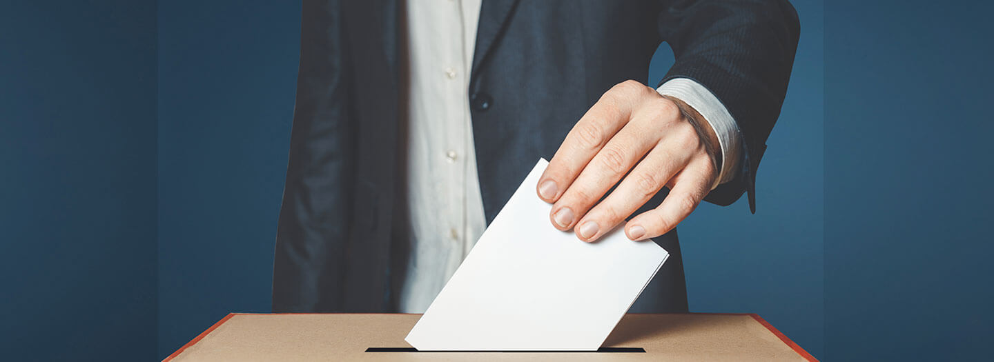 Closeup on a man's hand placing a ballot into a voting box