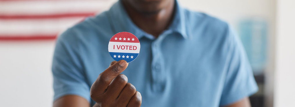 A man holds up a sticker that reads "I voted"