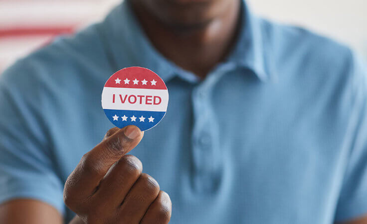 A man holds up a sticker that reads "I voted"