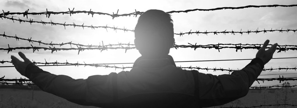 A man stretches his arm outward toward a barbed wire fence