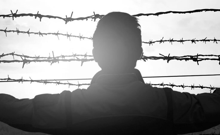 A man stretches his arm outward toward a barbed wire fence