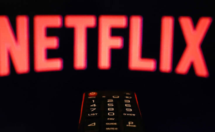 A TV remote control is aimed at a black screen displaying the Netflix logo