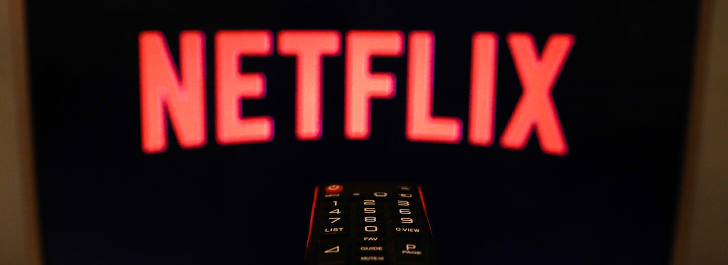 A TV remote control is aimed at a black screen displaying the Netflix logo
