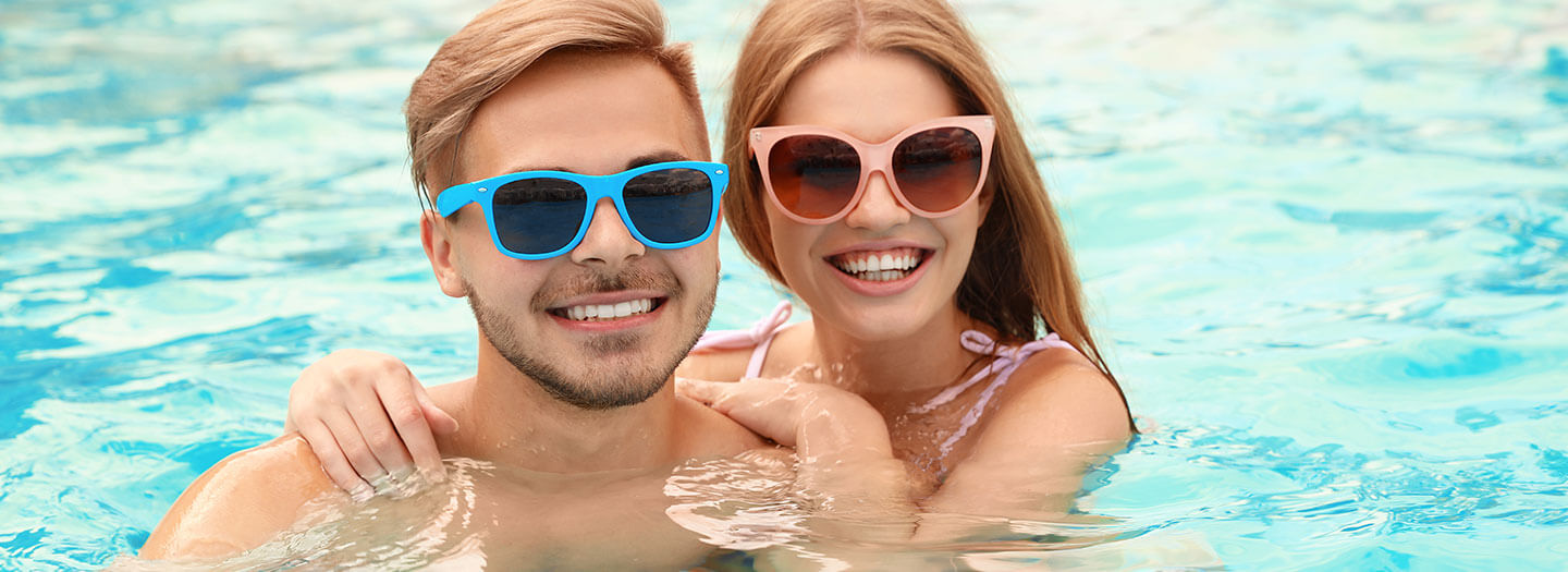 A man and woman, both wearing sunglasses, float in a pool while smiling for the camera