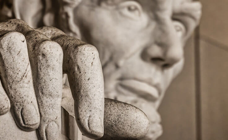 A closeup of a statue of Abraham Lincoln, focused on his hand with his face in the background