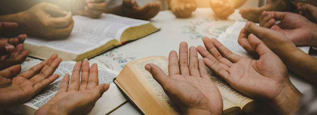 Open hands in prayer over Bibles