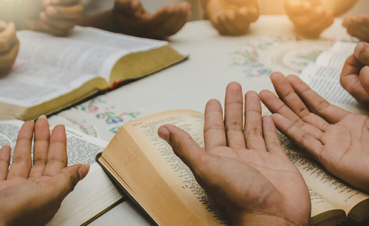 Open hands in prayer over Bibles