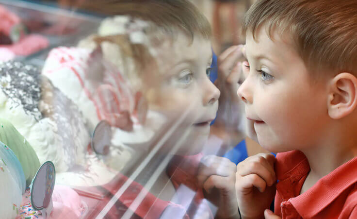 A boy looks at an assortment of ice cream behind a glass case