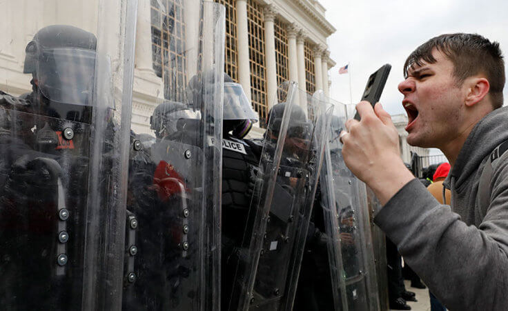 Police officers in riot gear stand guard while Trump supporters protest on the steps of U.S. Capitol in Washington on January 6, 2021.