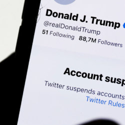 Donald Trump's Twitter account displayed on a phone screen and Twitter logo in the background