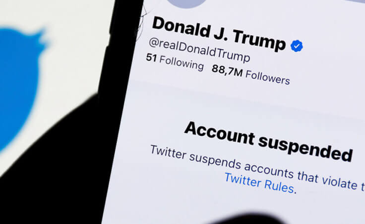 Donald Trump's Twitter account displayed on a phone screen and Twitter logo in the background