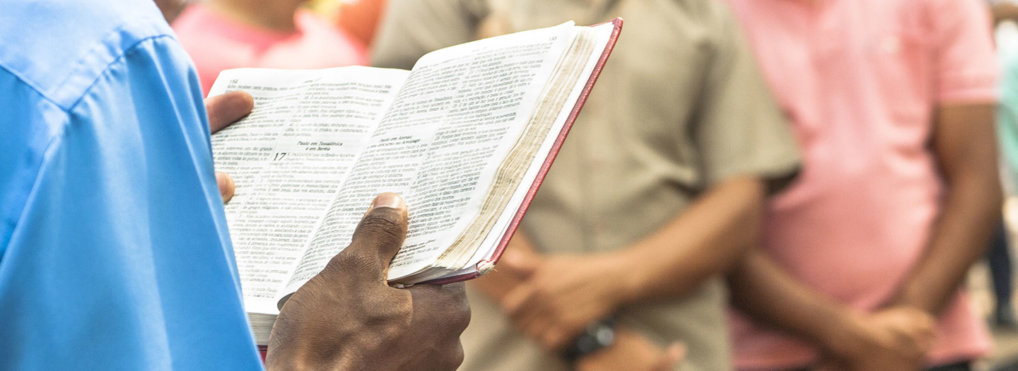 Close up on a man holding open a Bible in front of a few people