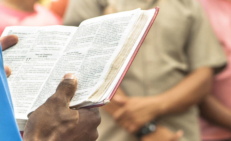 Close up on a man holding open a Bible in front of a few people