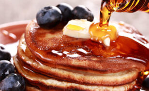 Syrup is poured over buttered pancakes, with blueberries surrounding