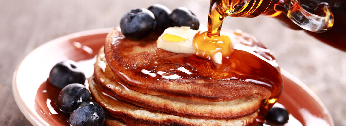 Syrup is poured over buttered pancakes, with blueberries surrounding