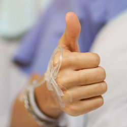 A close-up of a thumbs-up from a patient on a hospital bed