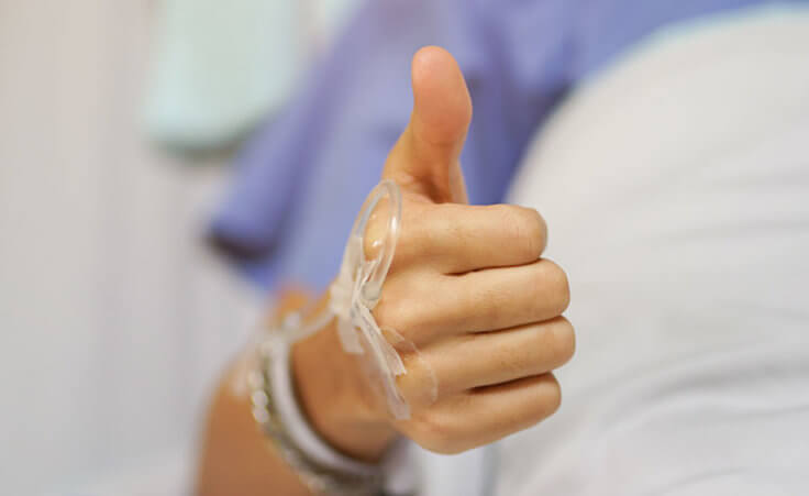 A close-up of a thumbs-up from a patient on a hospital bed