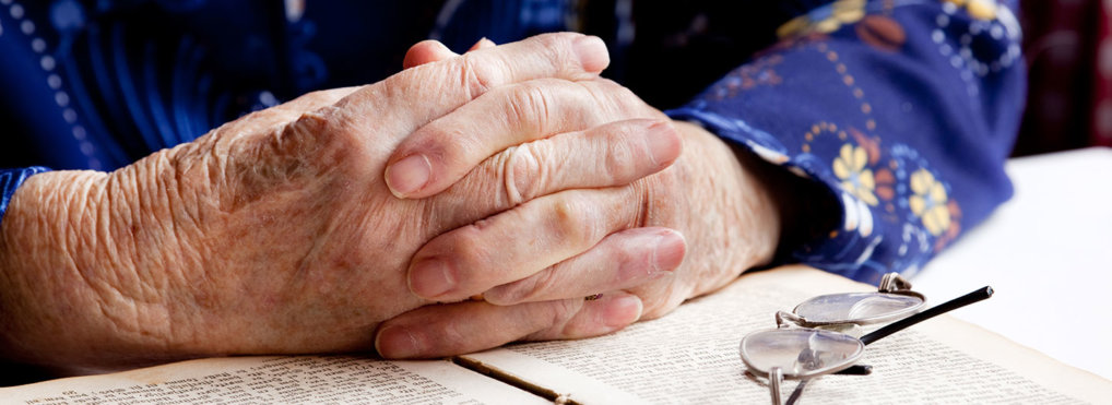close up of a senior adult's hands folded in prayer over a Bible