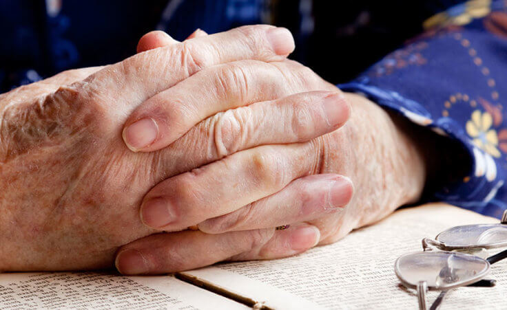 close up of a senior adult's hands folded in prayer over a Bible