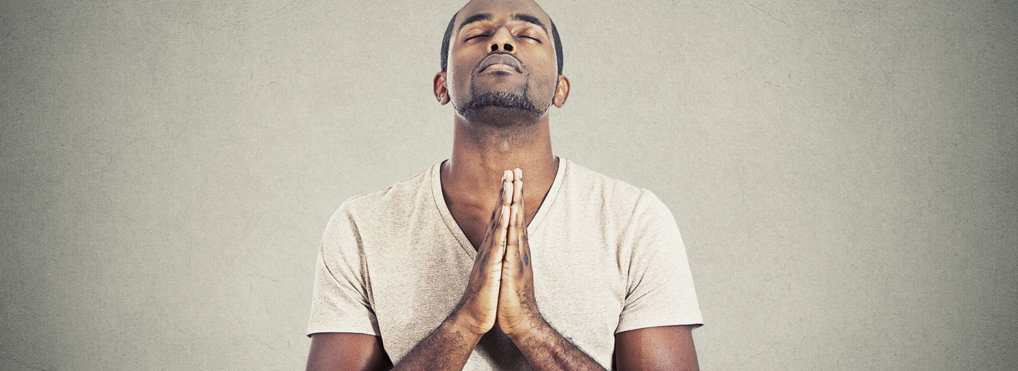 A man prays with his head looking up, eyes closed, hands clasped in prayer