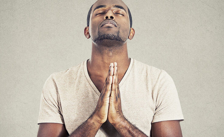 A man prays with his head looking up, eyes closed, hands clasped in prayer