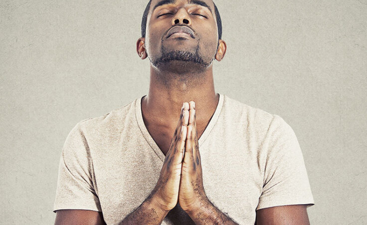A man prays with his head looking up, eyes closed, hands clasped in prayer