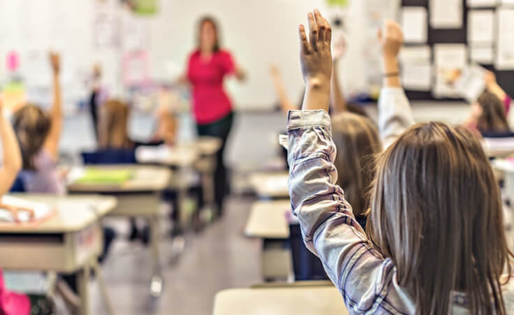 Children raise their hands inside of a classroom