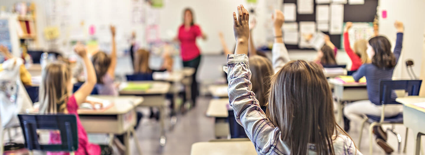 Children raise their hands inside of a classroom