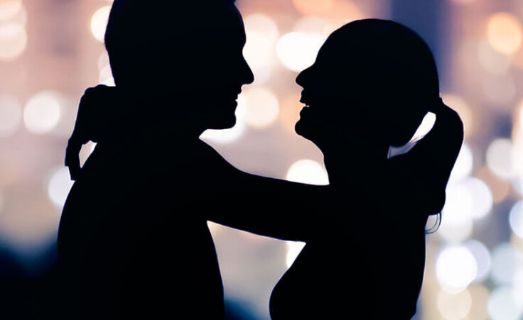 A woman lovingly drapes her arms around a man's neck