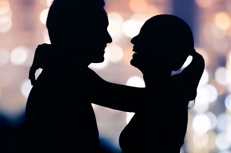 A woman lovingly drapes her arms around a man's neck