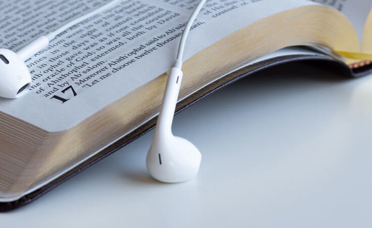 A pair of white white headphones lay on top of an open Bible
