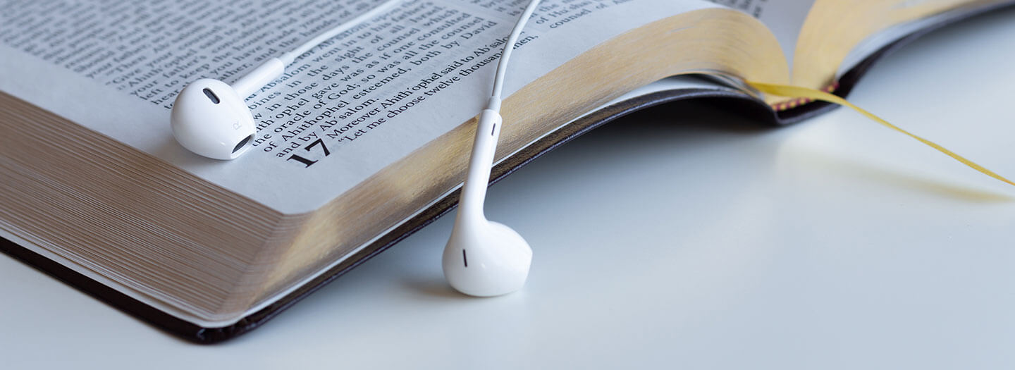 A pair of white white headphones lay on top of an open Bible