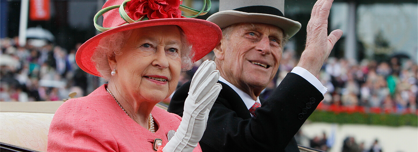 Queen Elizabeth and Prince Philip wave from a horse-drawn carriage.