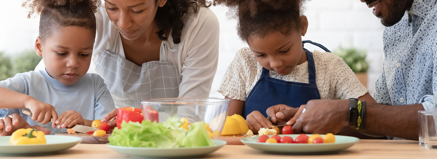 A mother and father with their daughters cut vegetables on a table