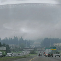 A UFO hovers within clouds above a busy highway
