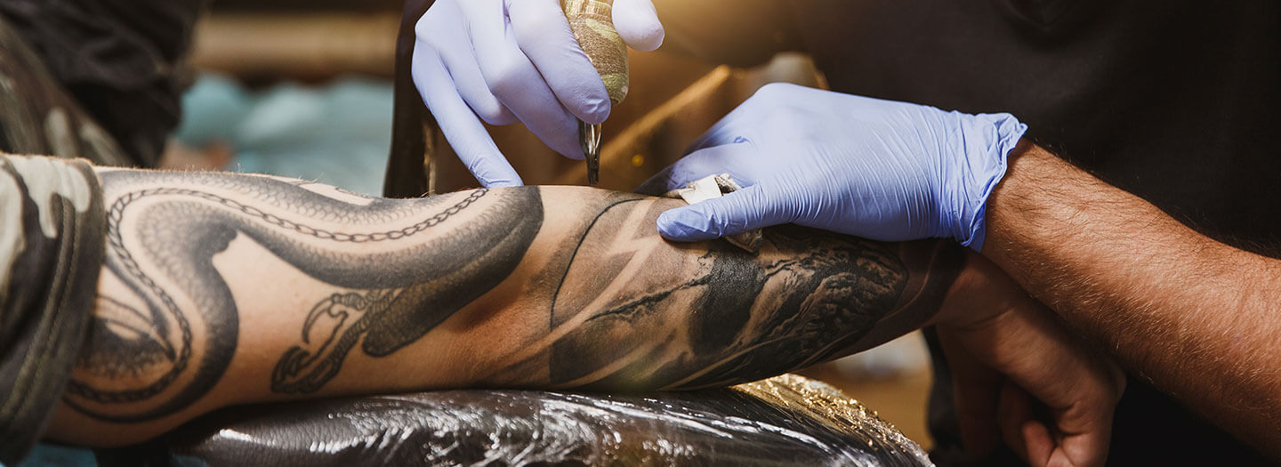 A tattoo artist works on an inked arm