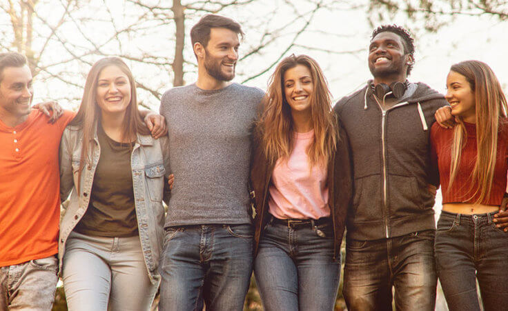 A diverse group of young people link arms in a park