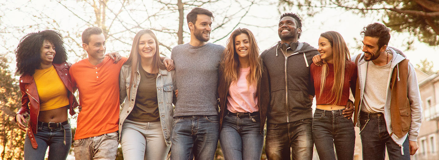 A diverse group of young people link arms in a park