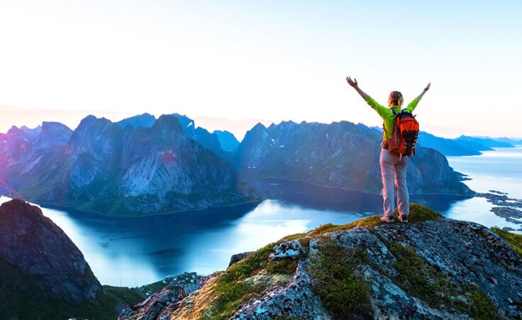 A hiker atop a mountain in Norway stretches our her arms