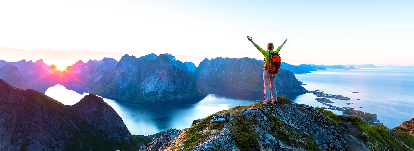 A hiker atop a mountain in Norway stretches our her arms